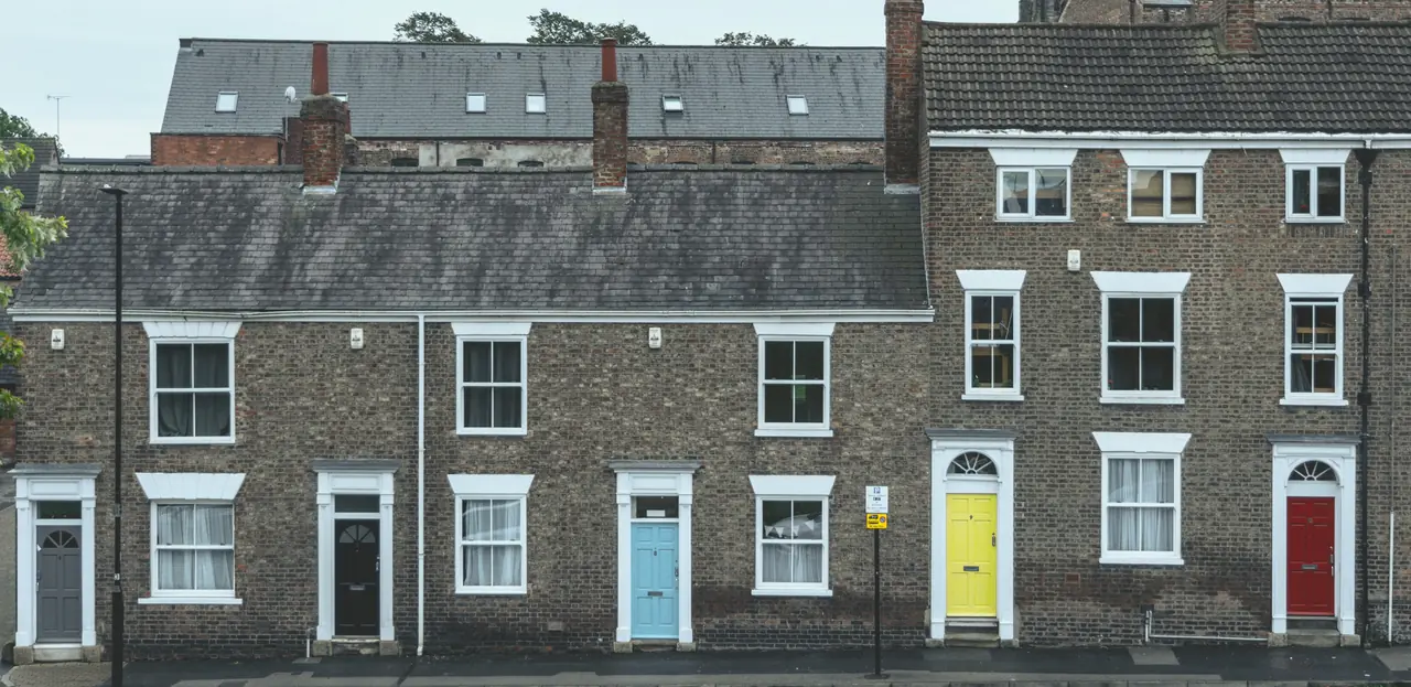 A row of brick terraced houses with sash windows and coloured front doors on a London street