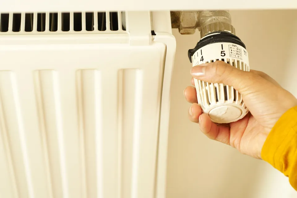 A hand adjusting the thermostatic valve on a white radiator
