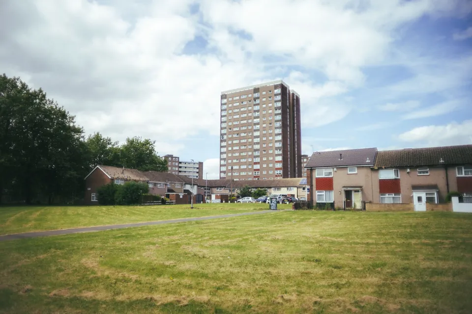 A tower block and low-rise homes beside an open green on a UK housing estate