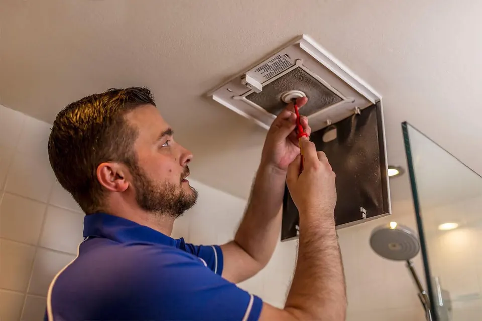 A technician fitting a bathroom extractor fan